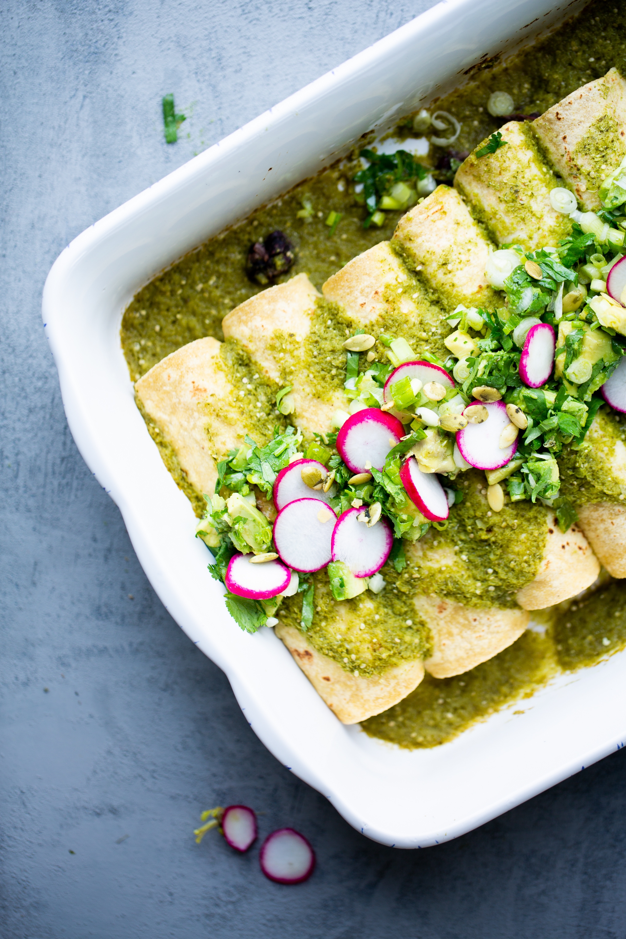 Enchiladas verdes casserole topped with diced avocado, cilantro and radishes.