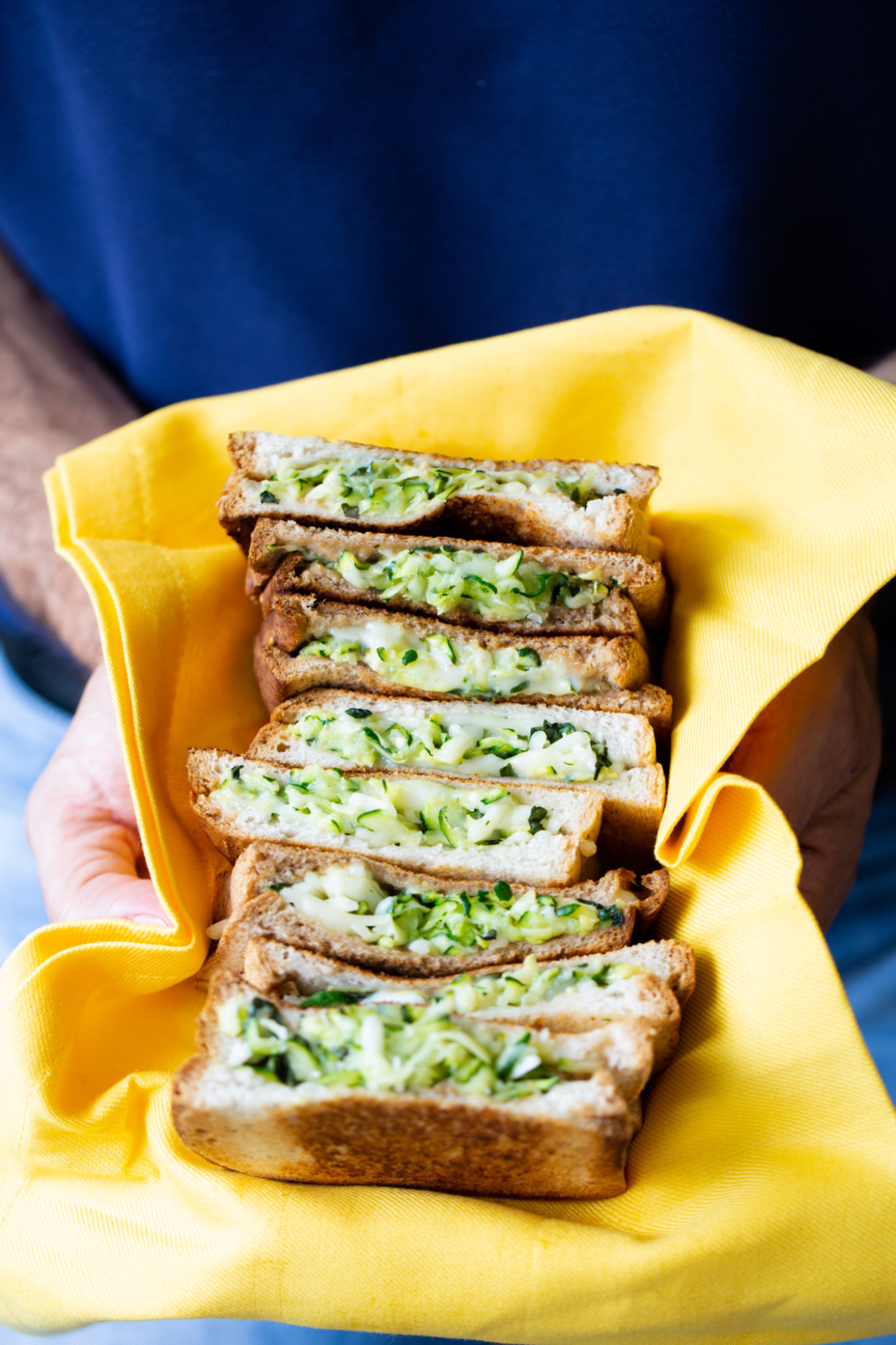 Zucchini sandwich on a yellow cloth napkin being held by a man.