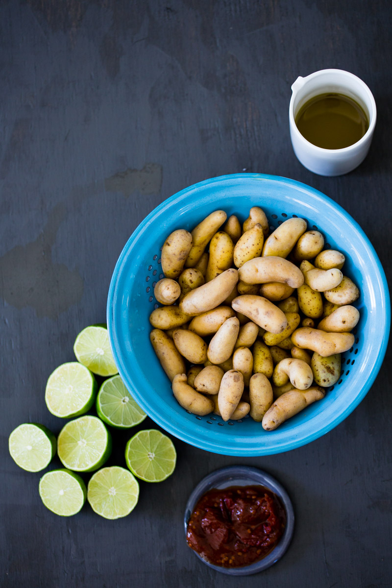 blue colander with small potatoes and limes and chipotle paste on the side.