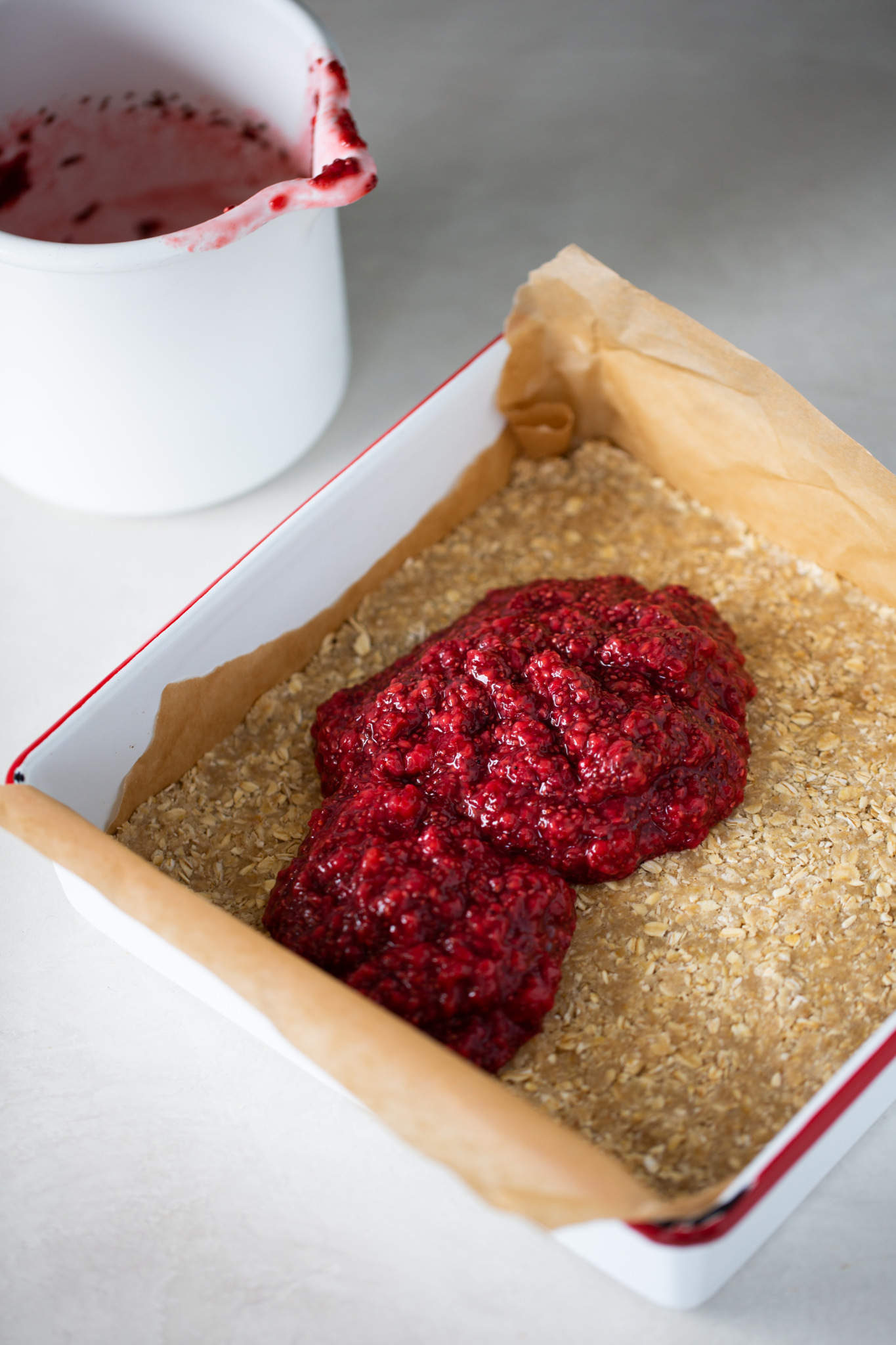 a square baking dish with one layer of oatmeal bar mix and raspberry chia seed jam on top.