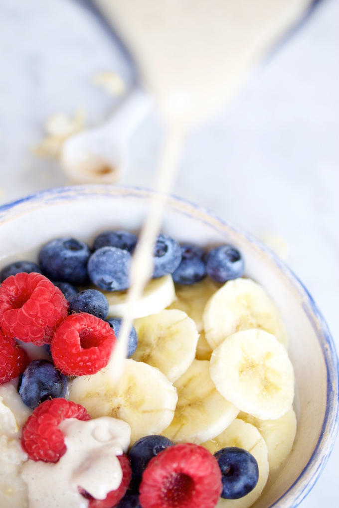 Pouring vegan cashew cream over oats and fresh berries