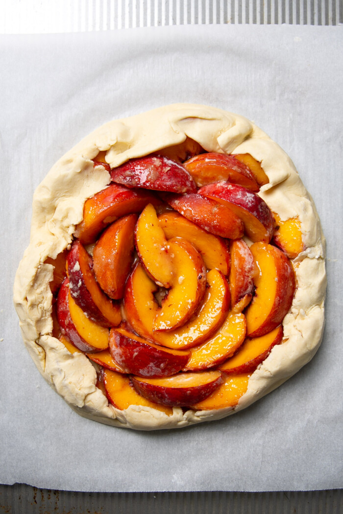 Peach galette before baking over a piece of parchment paper on a baking sheet.