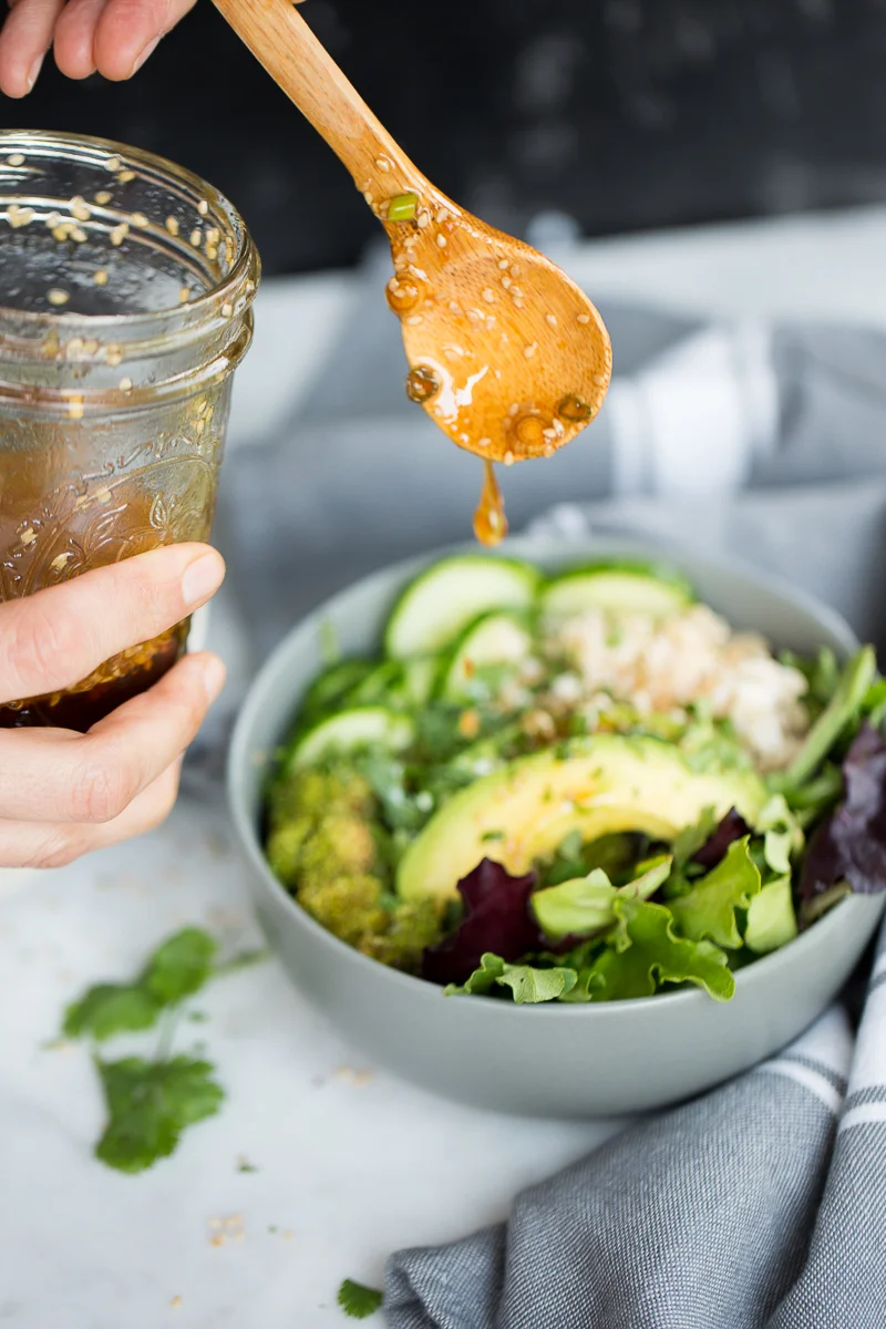 lime sesame dressing dropping over a greens and grains bowl