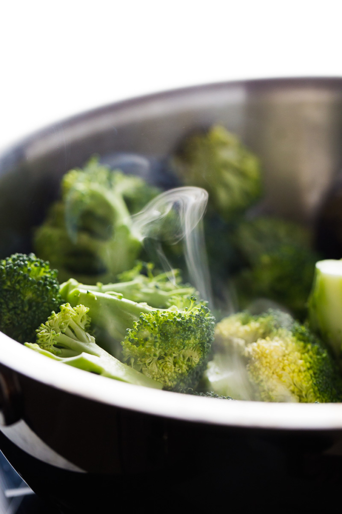 Steam coming out of a stainless steal pot with broccoli cooining.