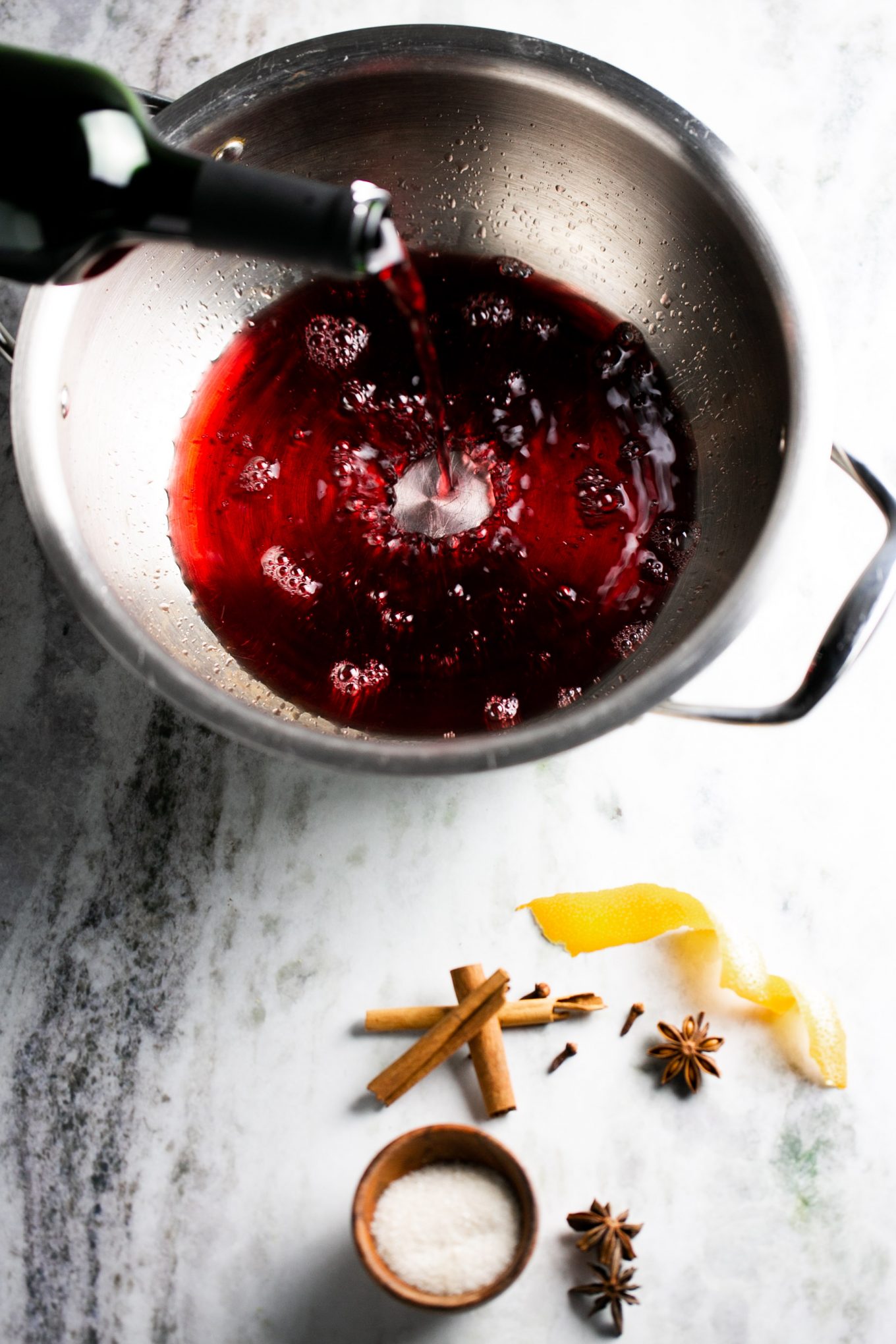 Pouring red wine into a stainless steal saucepot and ingredients on the side to make it.