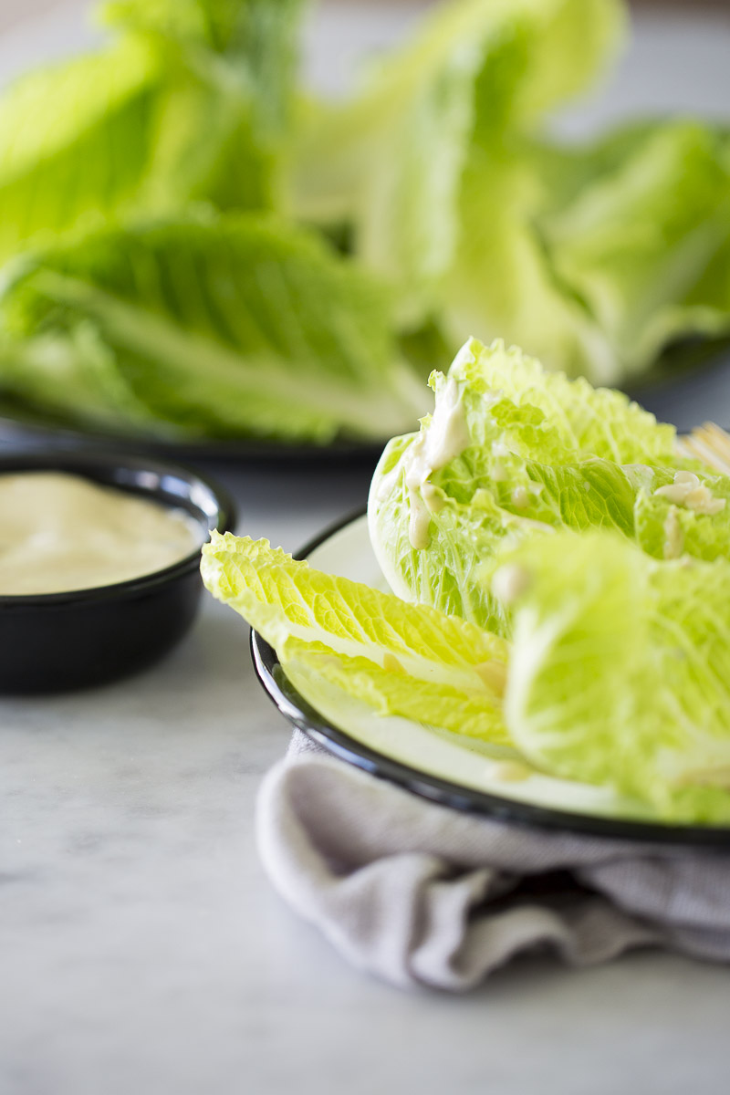Pouring creamy Caesar dressing without anchovies over romaine lettuce.