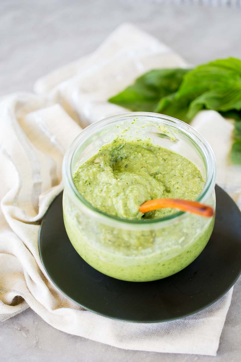 Avocado pesto in a wide mouth jar with a wooden spoon.