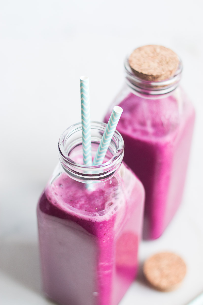 Pink beet smoothie in a glas s bottle with striped straw