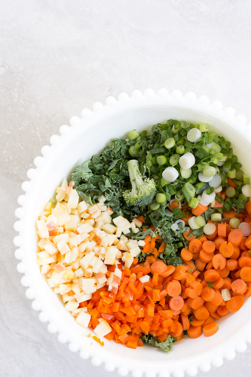 White salad bowl with crunch kale, brocoli, apples and carrots that make a perfect detox salad.
