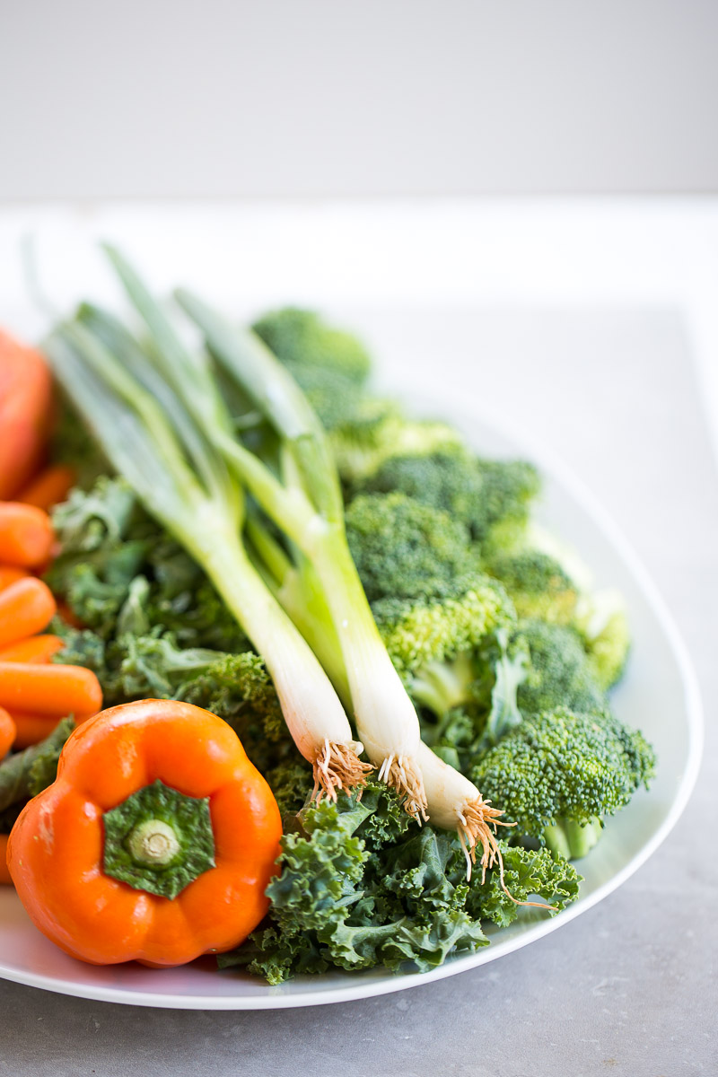 White platter with kale, scallions, orange bell pepper, broccoli and carrots.
