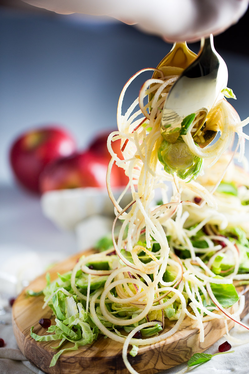 apple and brussel sprout salad being served with gold serving silverware.