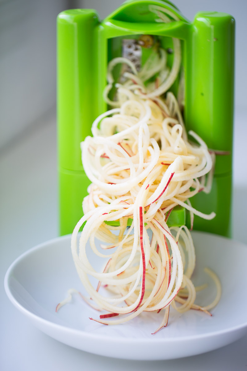 a spiralized apple being spiralized in a green spiralizer.