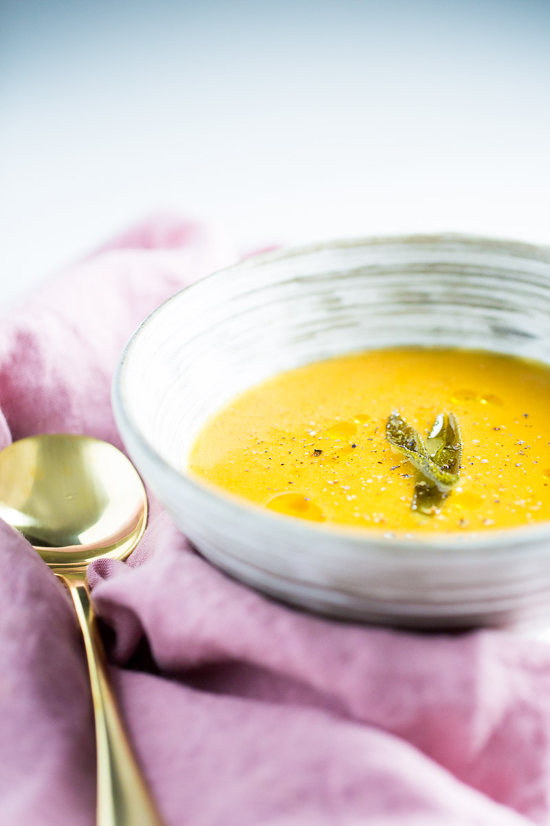 A bowl of vegan roasted butternut squash soup with a sprig of sage.