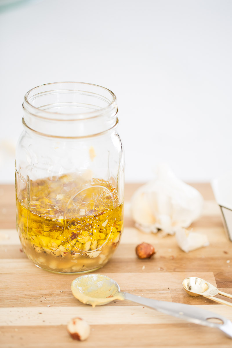 A jar of olive oil and a spoon creating a simple vinaigrette on a cutting board.