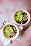 Two bowls of black bean soup on a pink background.