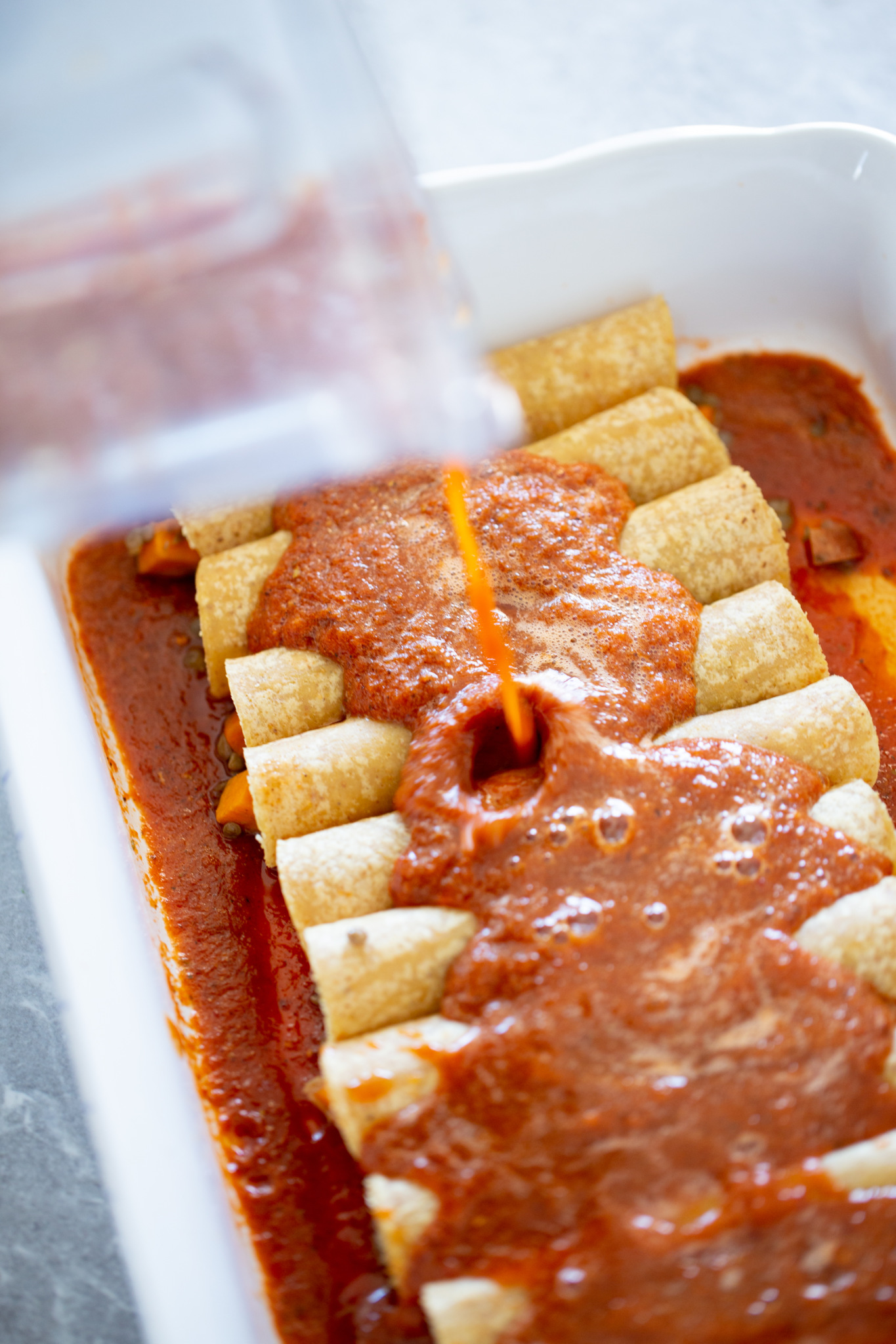 enchilada sauce being poured over enchiladas