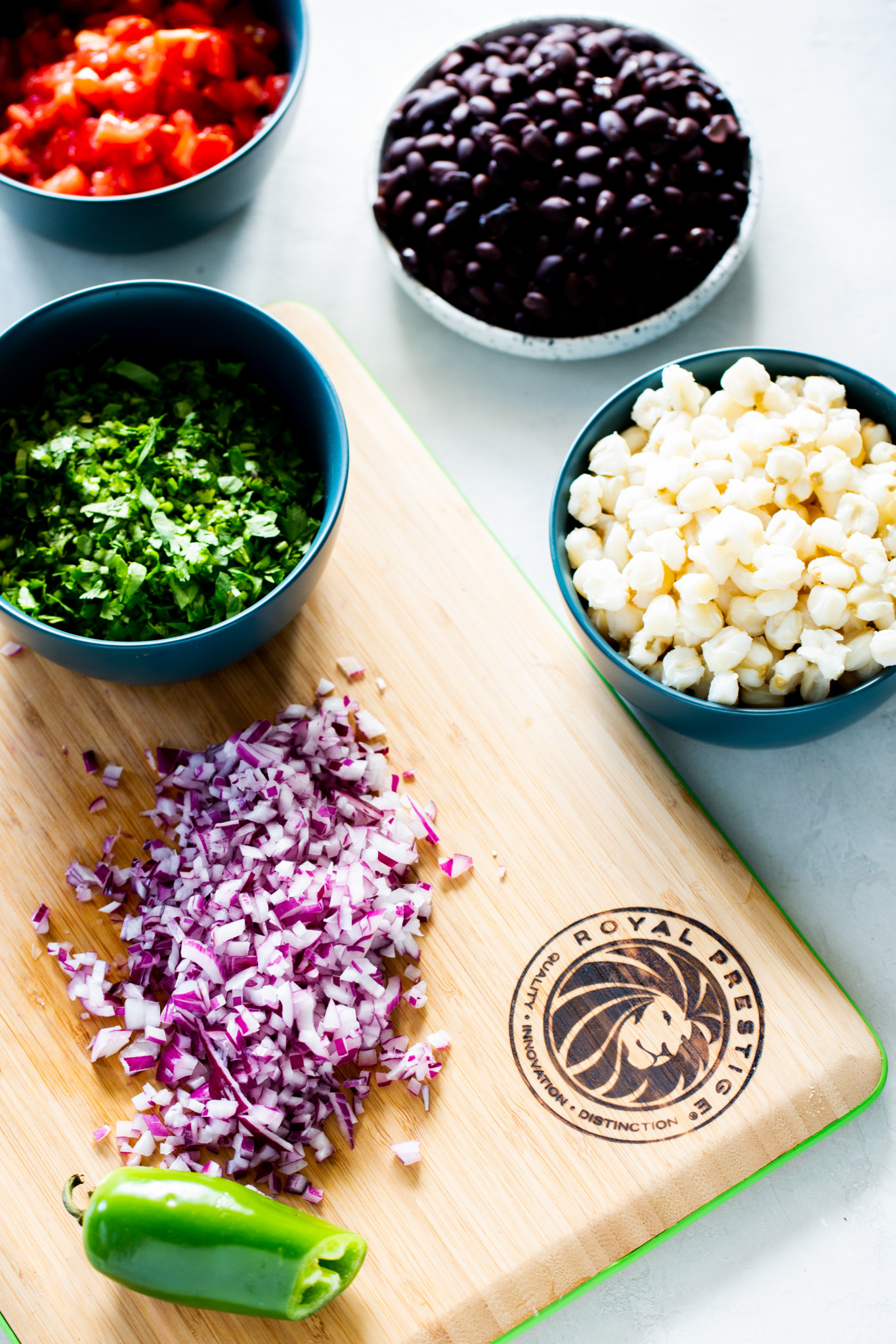 chopped red onion on board, black beans, avocado, corn, corn and pepitas in individual bowls.