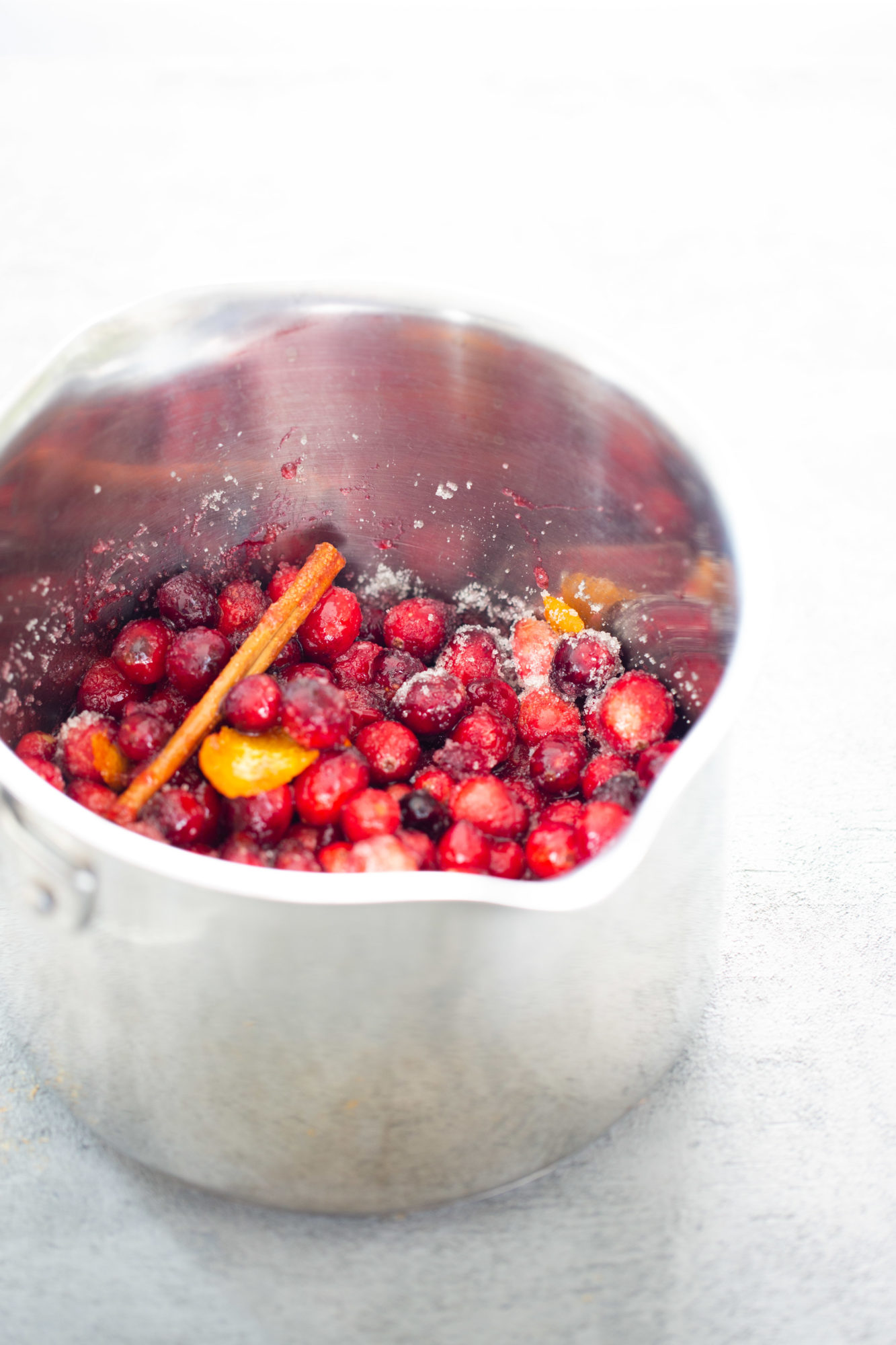 cranberries, sugra orange zest and a cinnamon stick in a sauce pot.