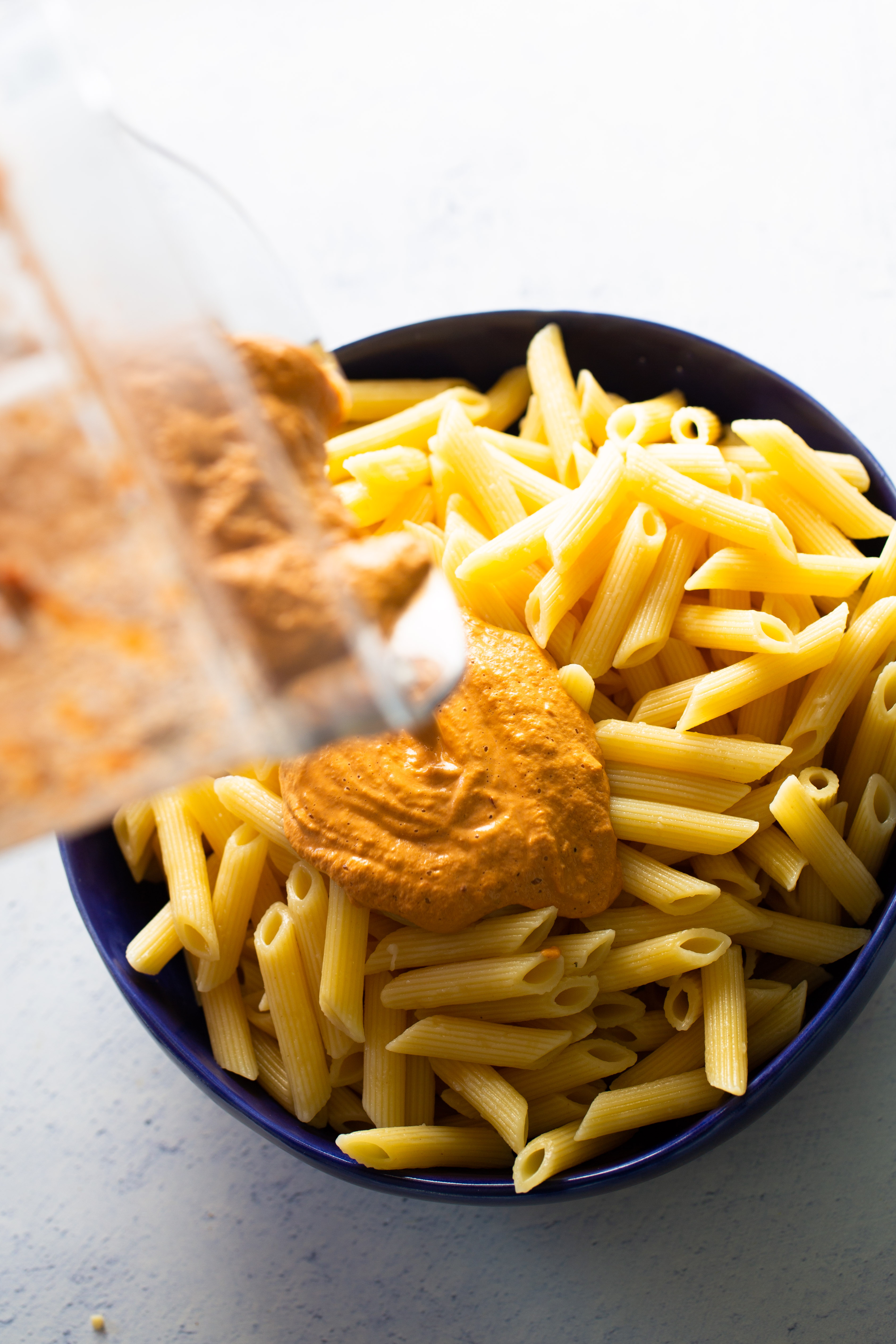 red pepper sauce being poured over pasta