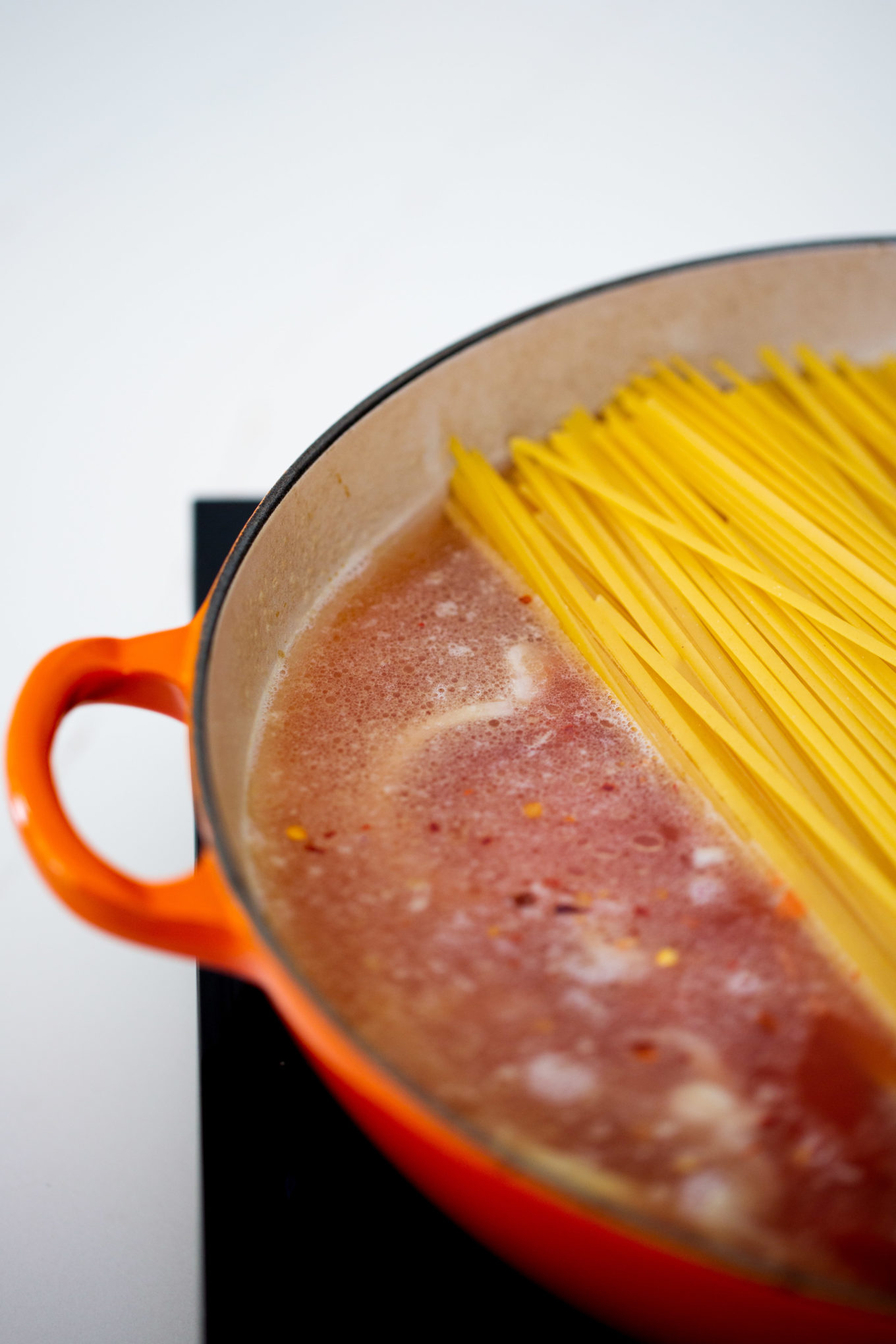 Pasta in a pan being cooked in an orange cast iron pan