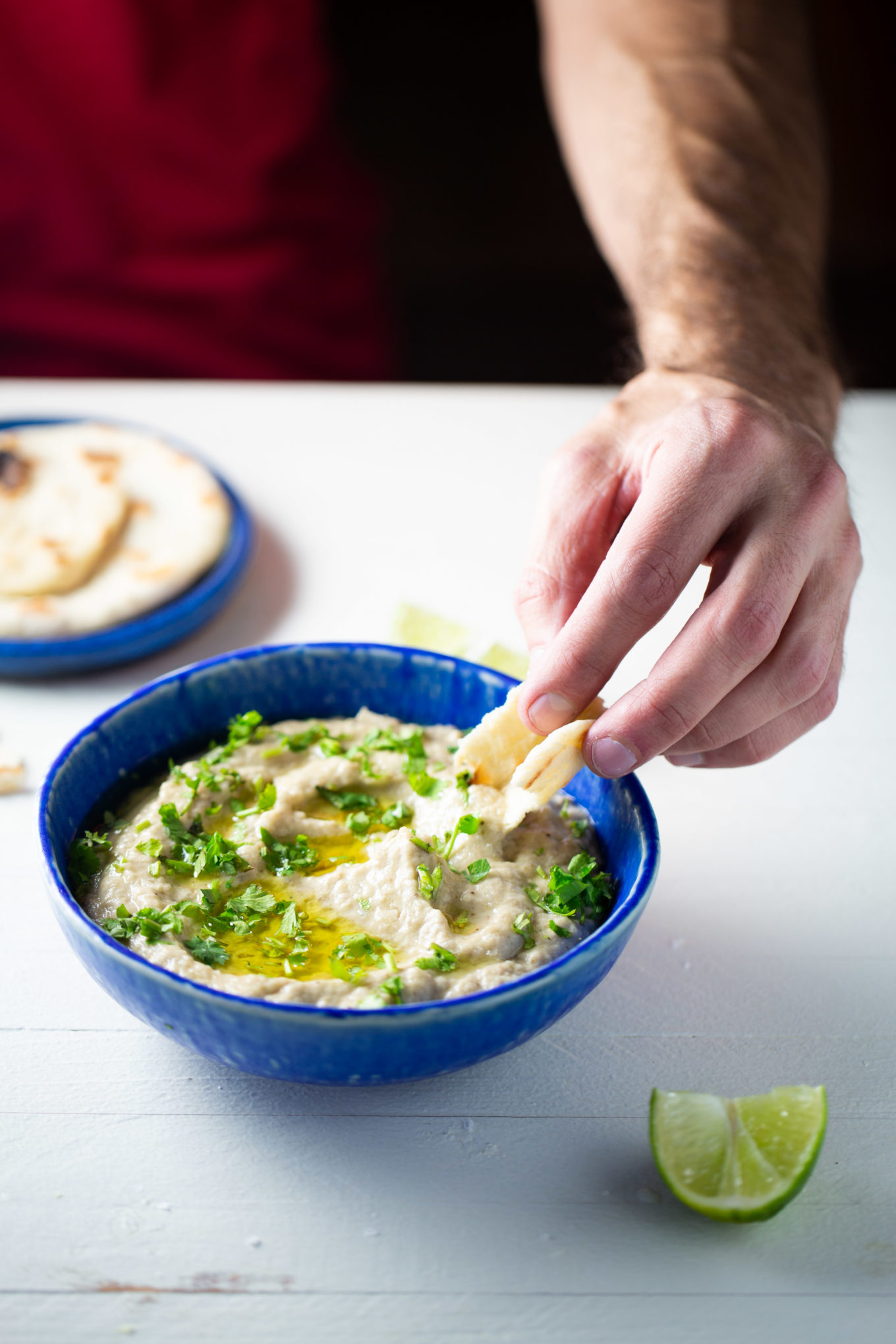 baba ghanoush in a blue bowl drizzled with olive oil and being scooped with pita breatd. with pita