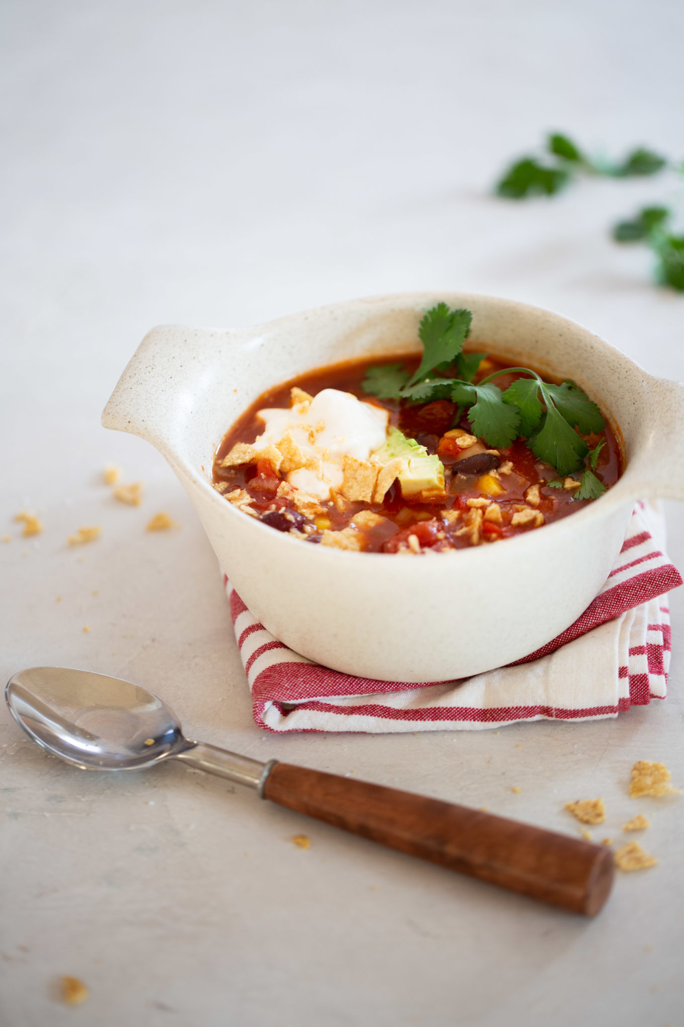 Three bean chili in a bowl served with cilantro, avocado and cream