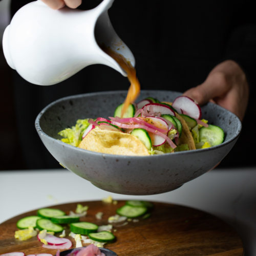 Sauce being poured over tacos dorados