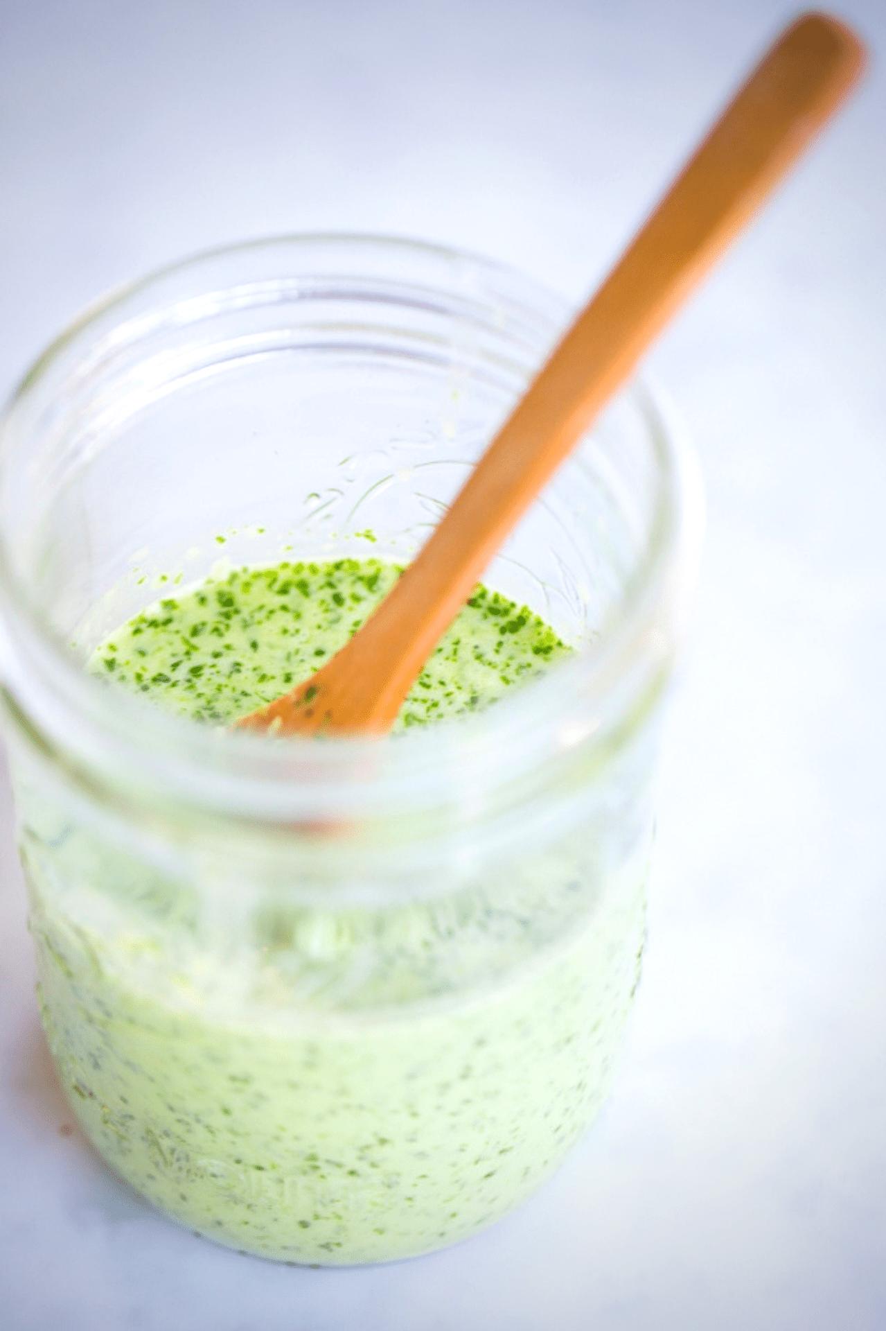 A jar of cilantro dressing with a wooden spoon.