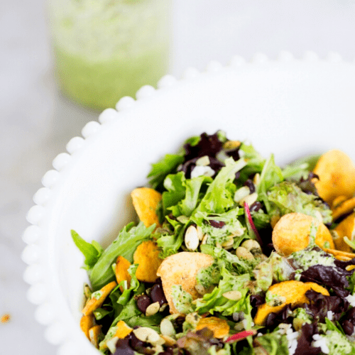A white bowl with a salad in it drizzled with cilantro dressing.