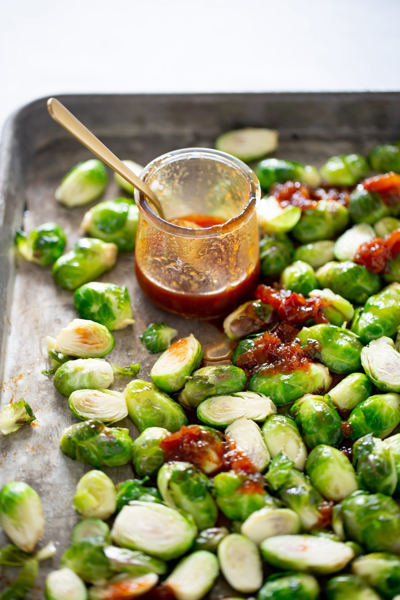 brussels spsrouts over baking sheet covered with sweet and spicy sauce.