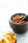 Red salsa served in a traditional stone bowl with crispy tortilla chips.