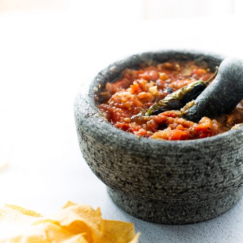 Red salsa served in a traditional stone bowl with crispy tortilla chips.