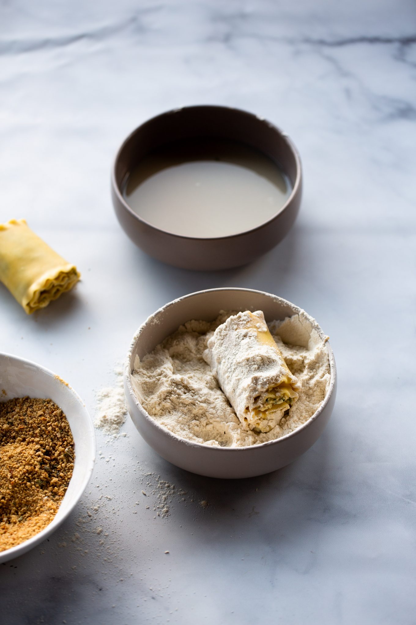 lasagna roll being dredge in a bowl full of flour