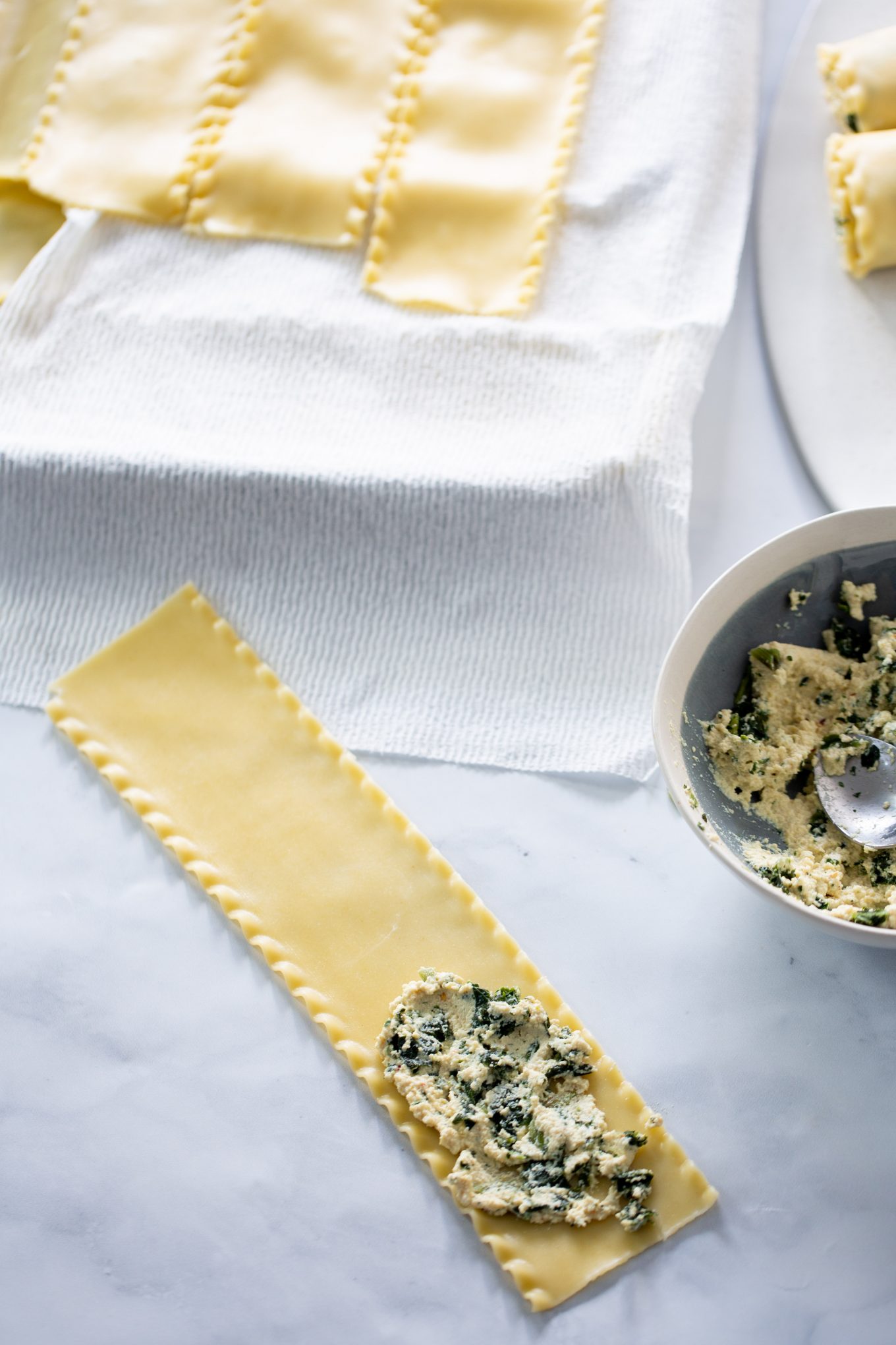 lasagna noodle over counter top  being filled with vegan ricotta and spinach