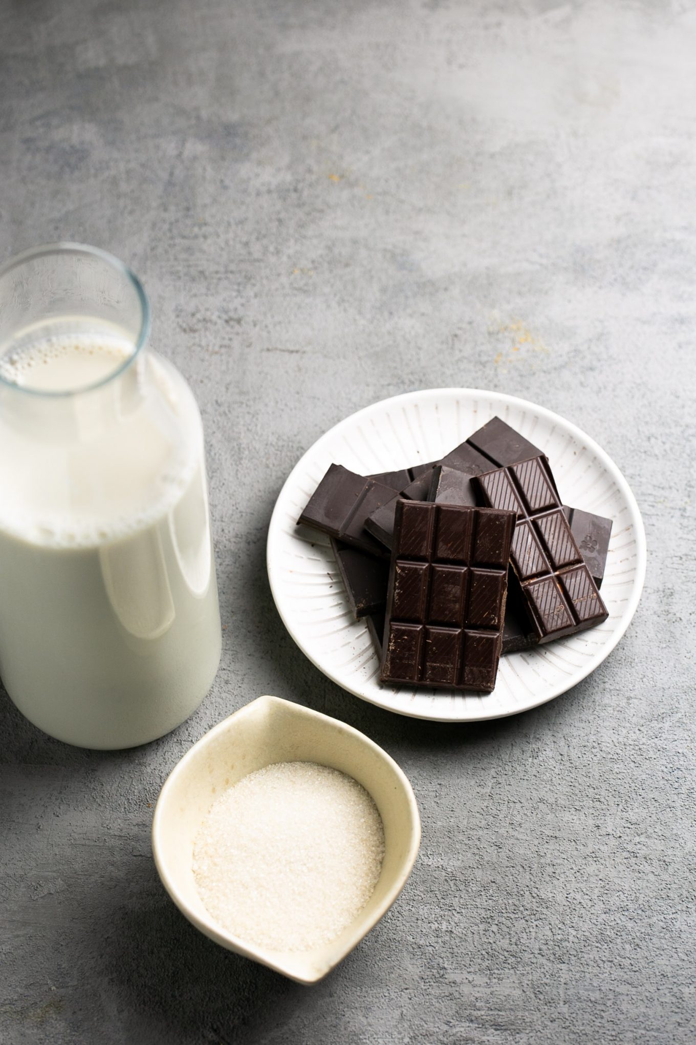 a bottle of milk, a small bowl with sugarn and a small plate with chocolate pieces.