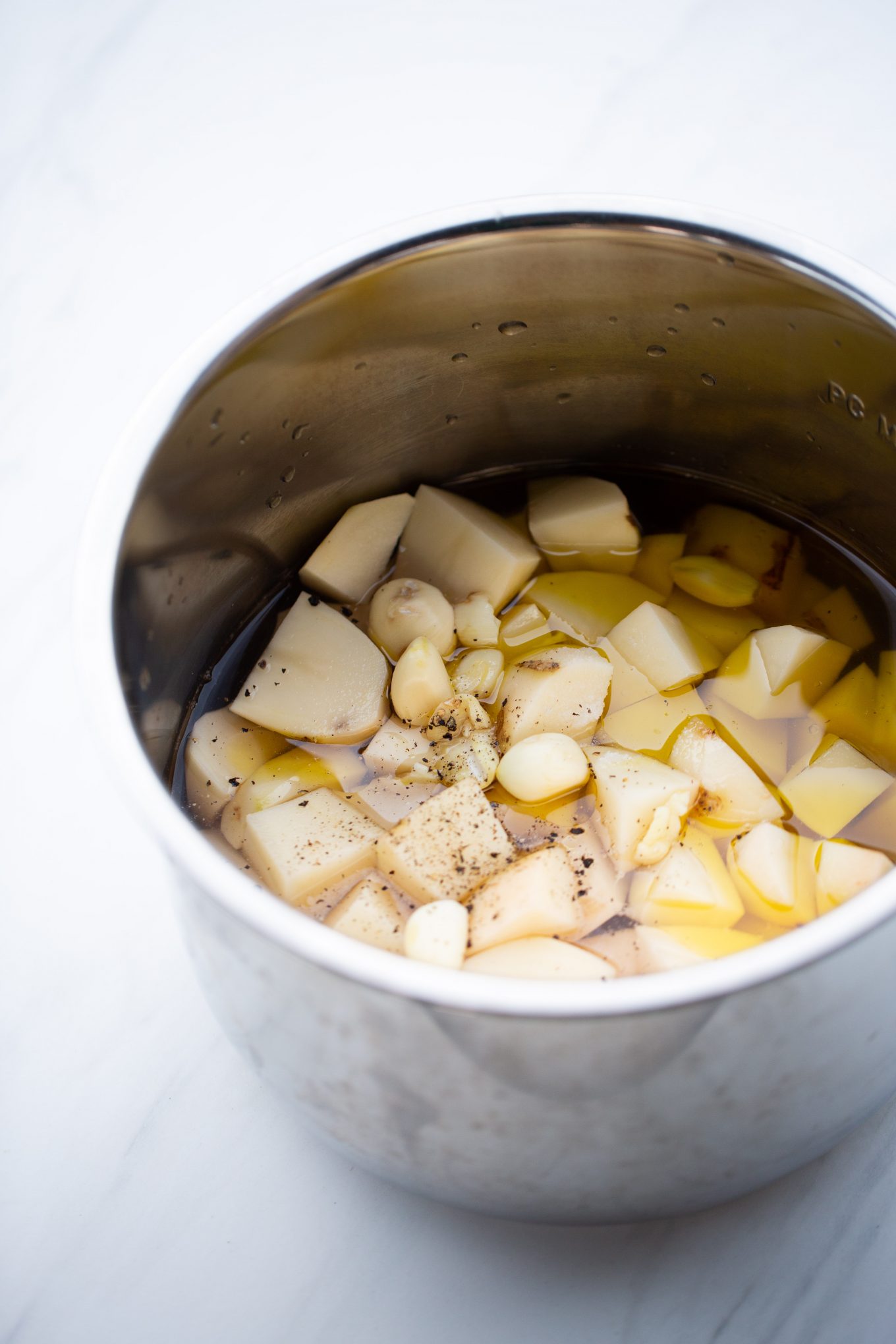 cubed potatoes in instantpot container with garlic cloves and pepper