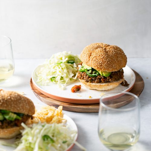 Two plates with sloppy joes and a glass of wine.