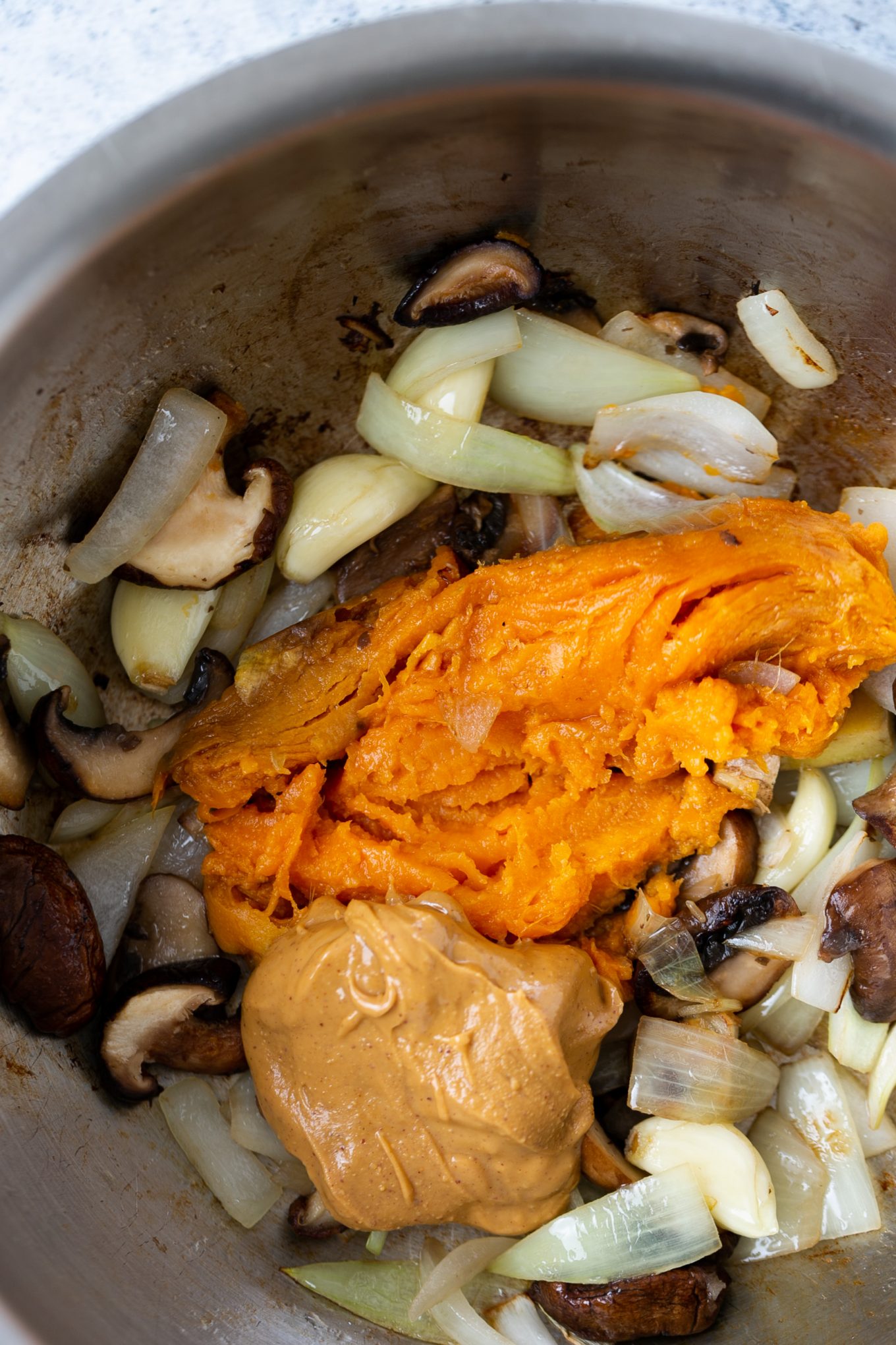 mushrooms, onion, garlic and ginger being sauteed in a pot and sweet potato and creamy peanut butter