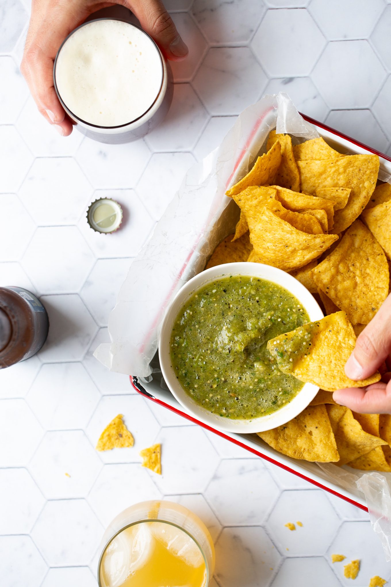 A bowl of mexican salsa verde with chips and a beer