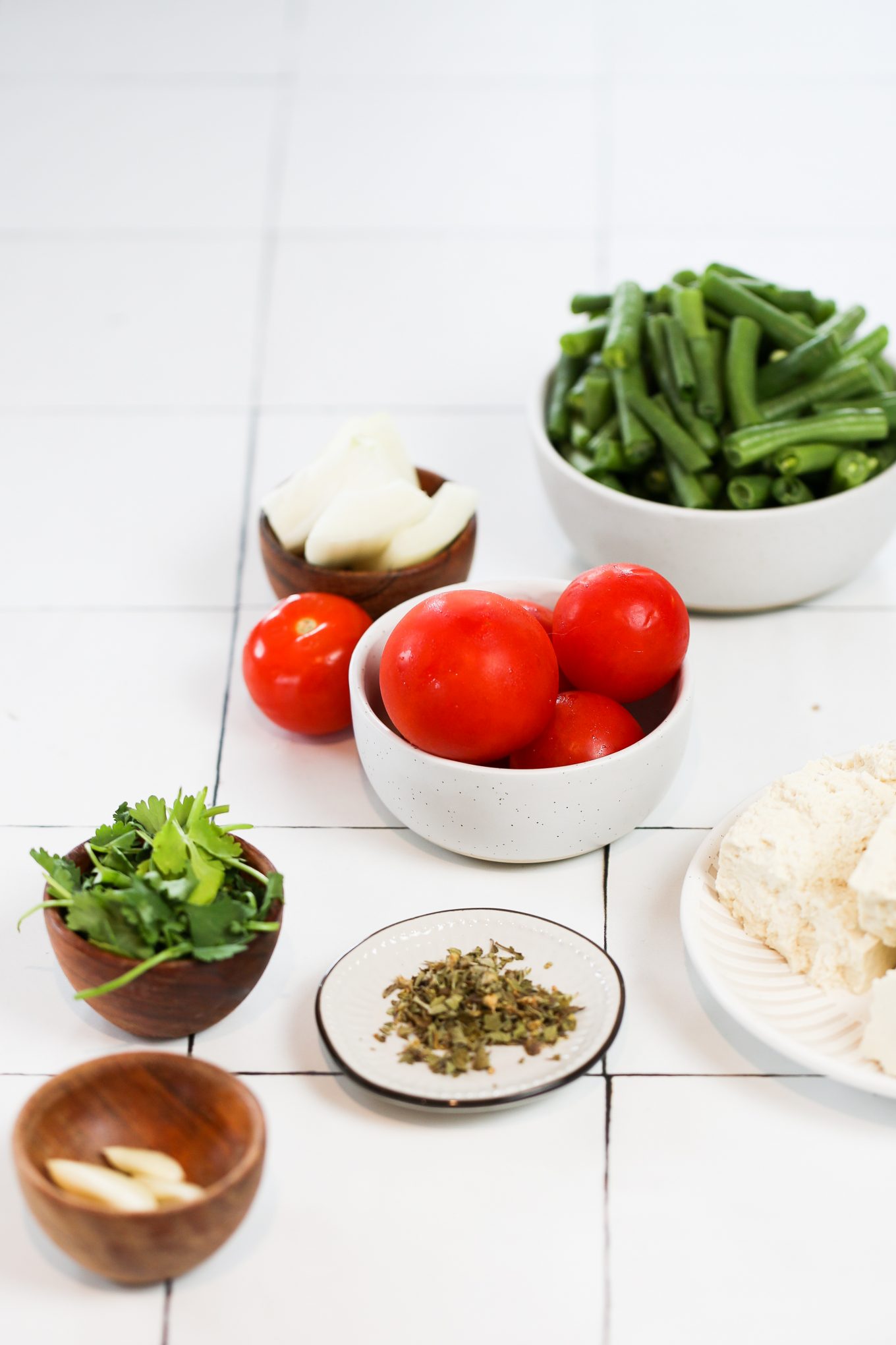 Tomatoes, cilantro, oregano, onion, garlic, tofu, green beans in bowls.