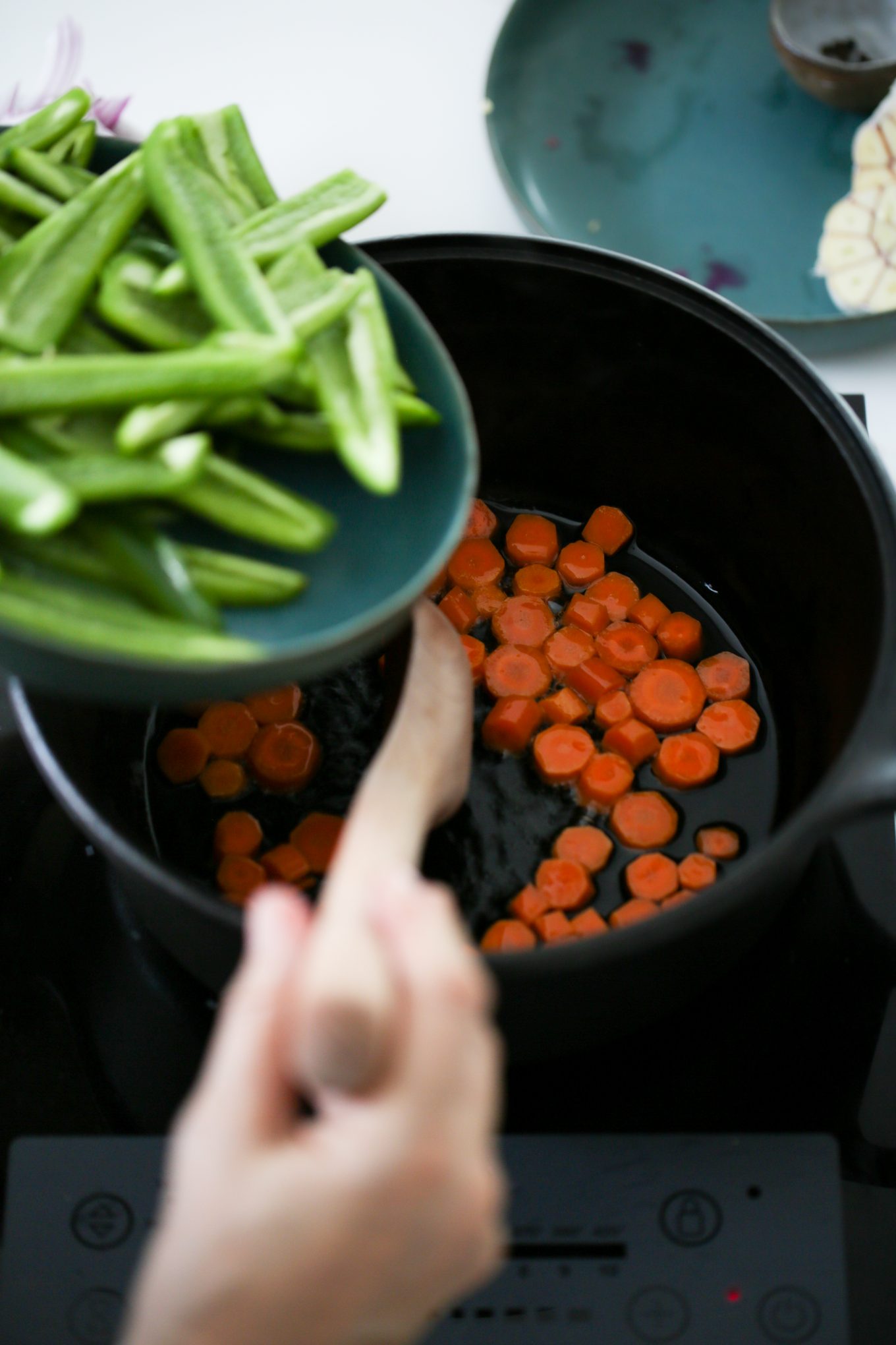 adding chiles jalapeños to a cast iron dutch oven with carrots in oil