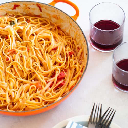 one pot pasta with tomatoes and onions in a brasier with two glasses with red wine on the side