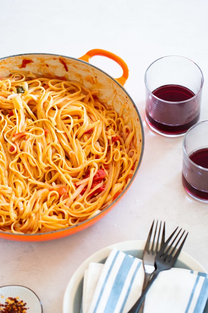 one pot pasta with tomatoes and onions in a brasier with two glasses with red wine on the side