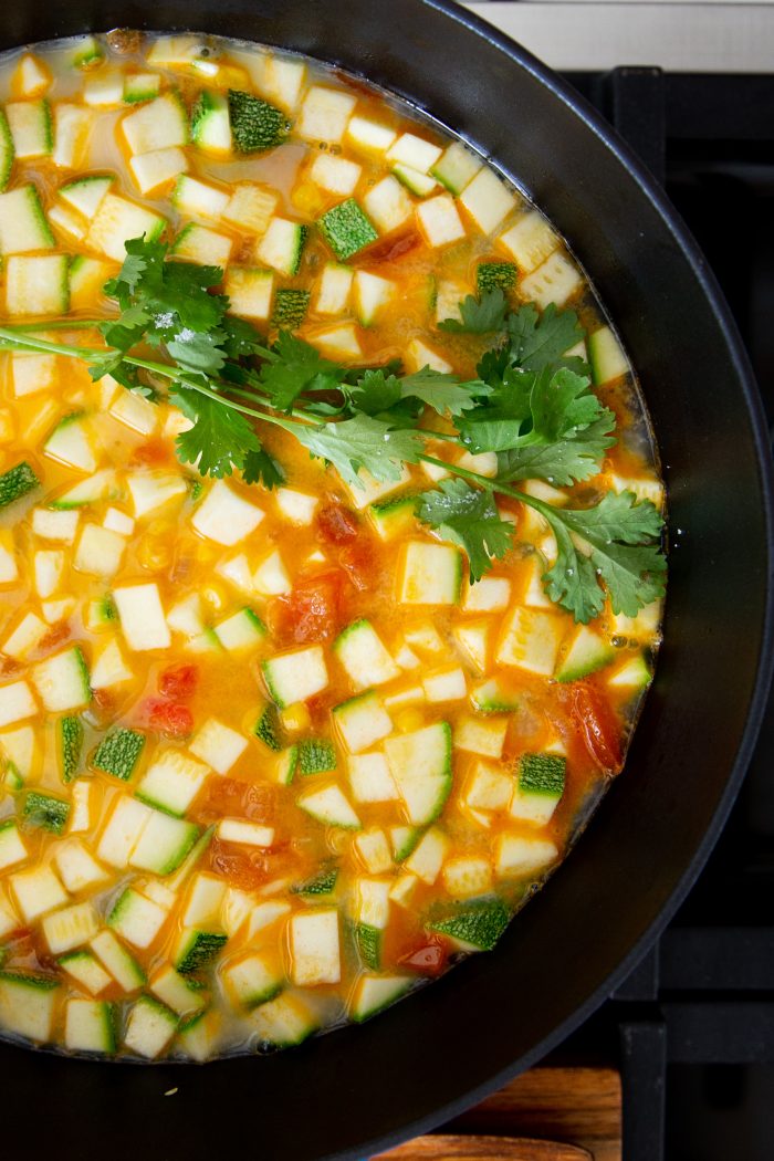 Overview of a a dutch oven with calabacitas, corn and tomato soup with a sprig of fresh cilantro