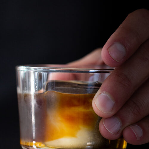 A person holding a glass with ice and carajillo in it.