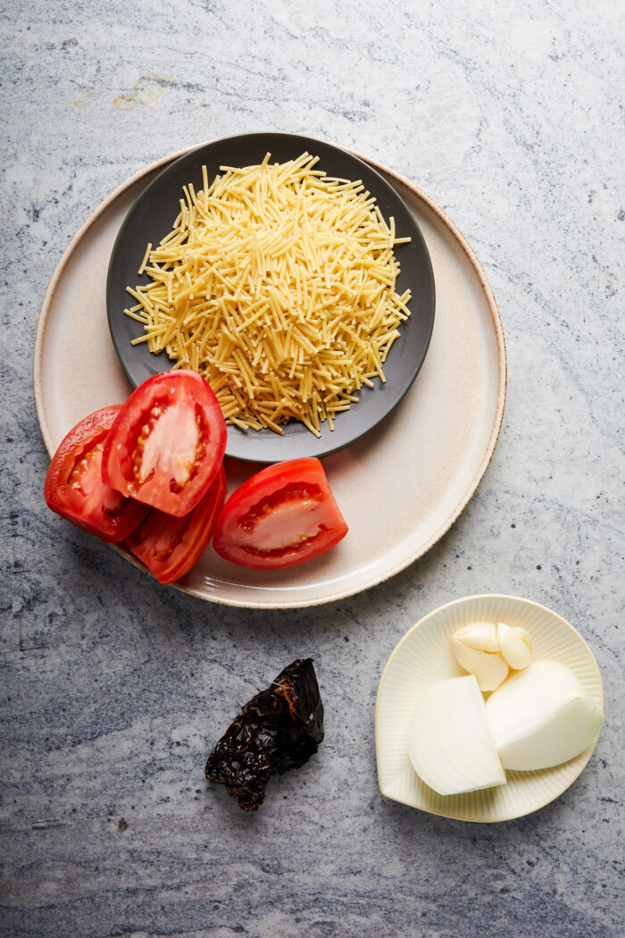 A plate of pasta and tomatoes on a marble table.
