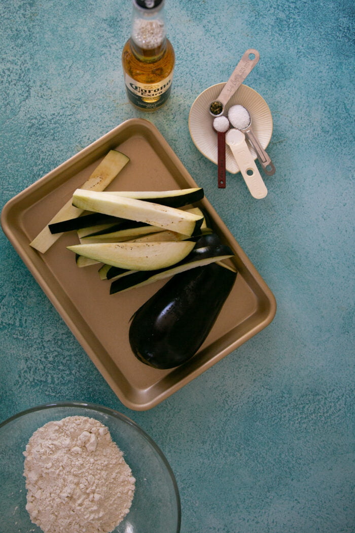 sliced eggplant on a baking sheet with meassured spices on the side to make a vegan fish taco recipe.