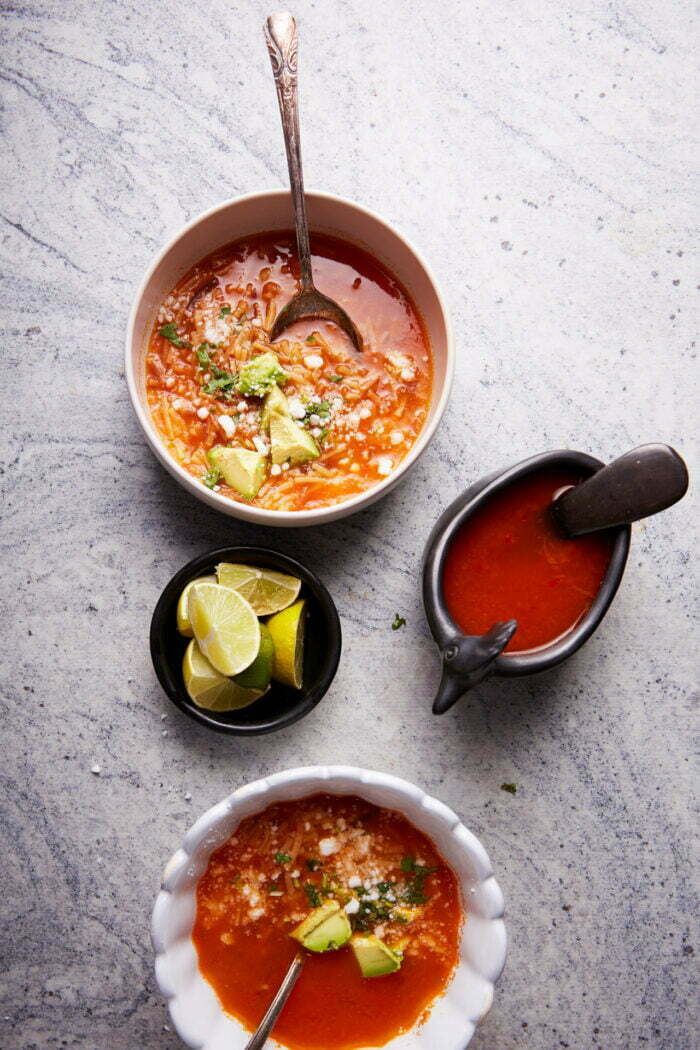 two bowls of sopa de fideo with abowl with limes and salsa.