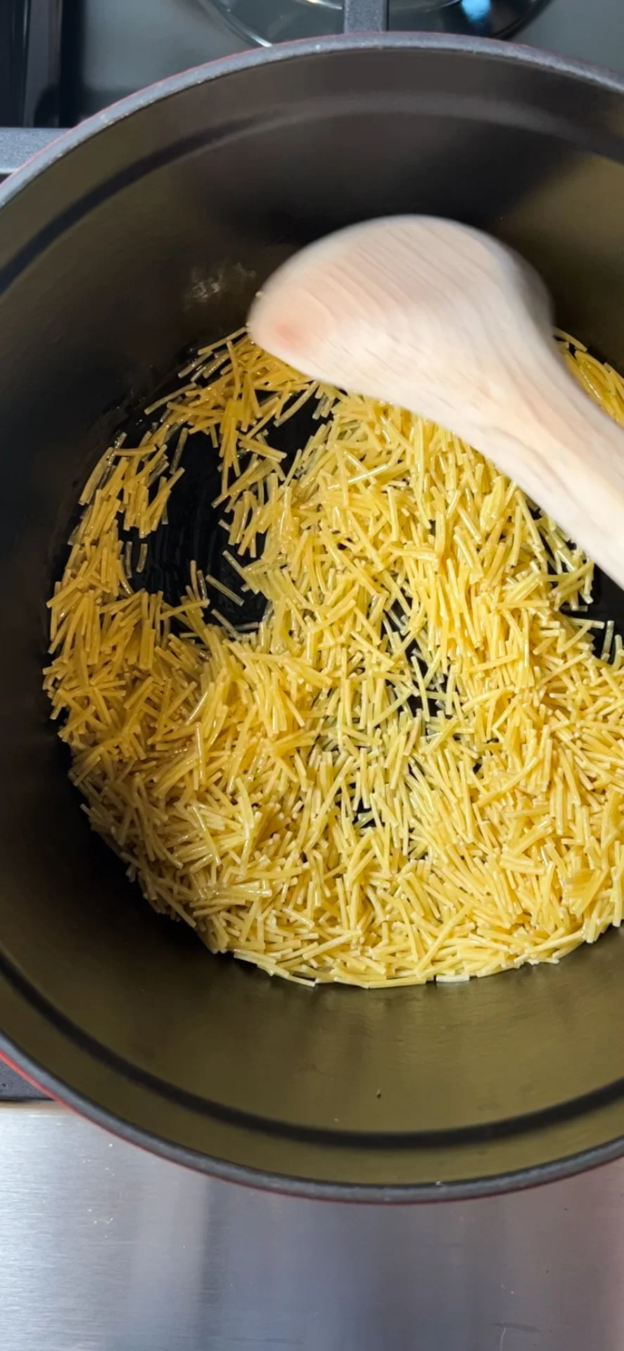 Fideo noodles being stirred in a pot before toasting.