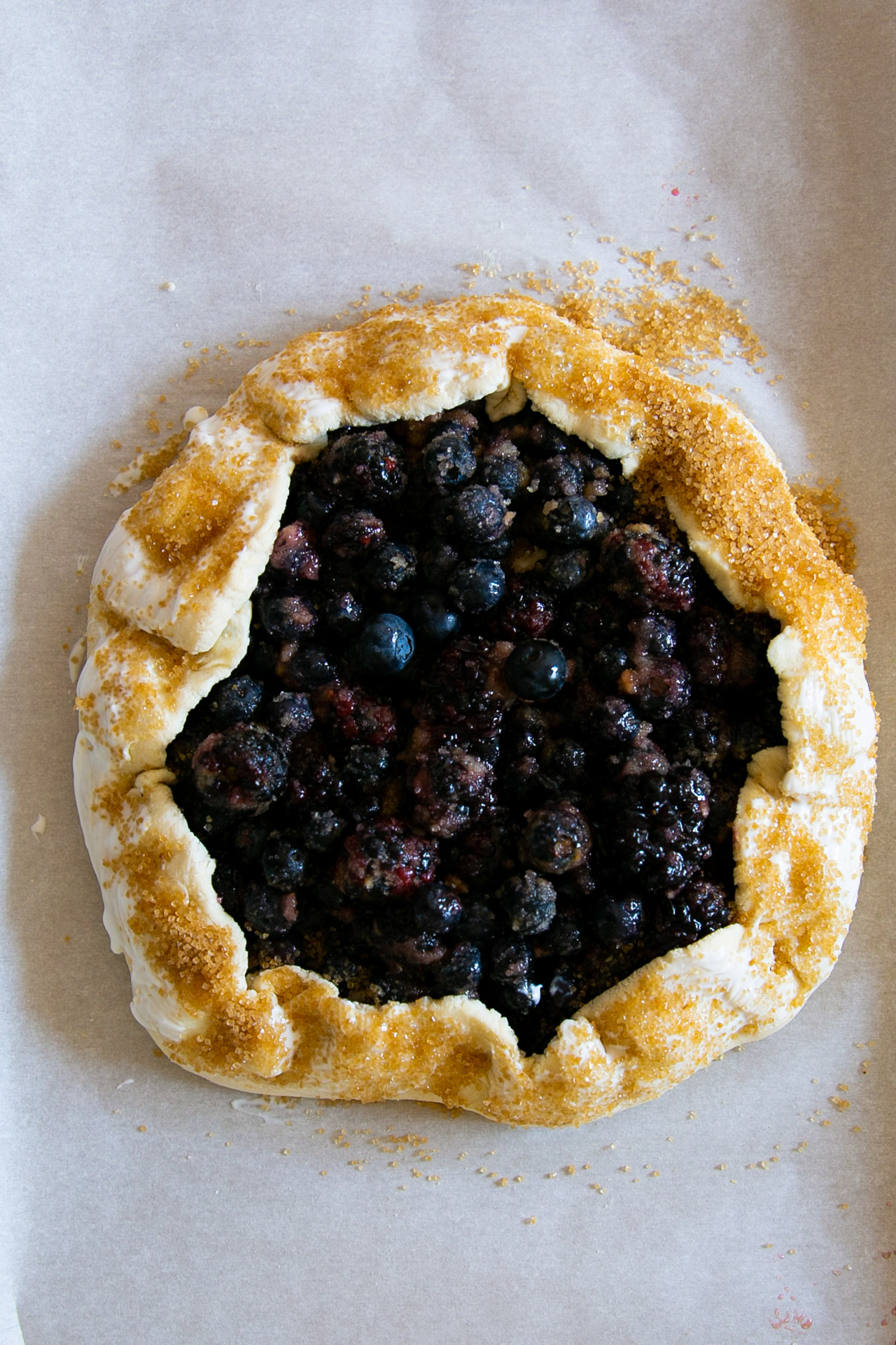 Baked vegan mixed berry galette, golden and bubbly, on parchment paper.